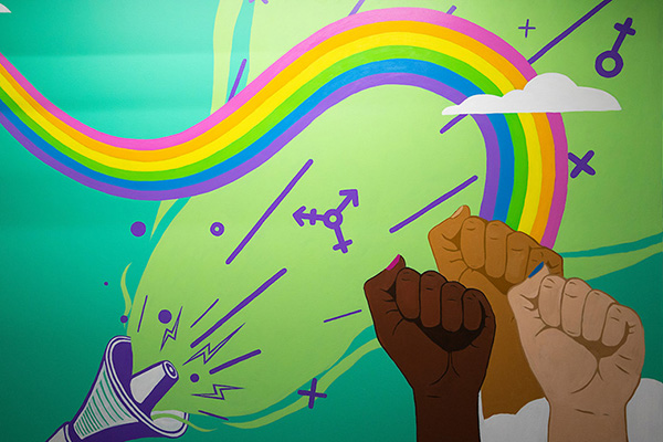 a colorful painted sign with a rainbow, bull horn, and clenched fists rising in solidarity