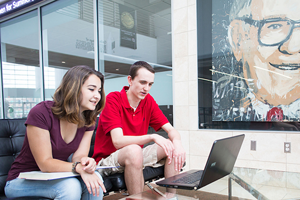 two uno students look at a laptop in the lobby of mammel hall on scott campus