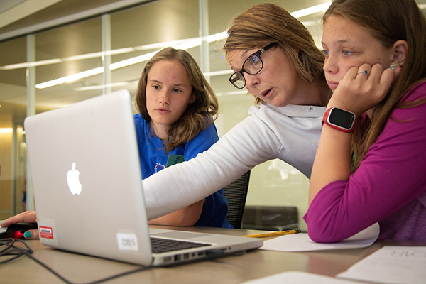 a teacher points to a laptop as she teaches two students