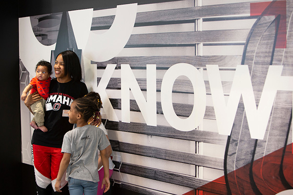 a woman in a uno shirt holds a baby and is surround by her children at a graduation reception at uno