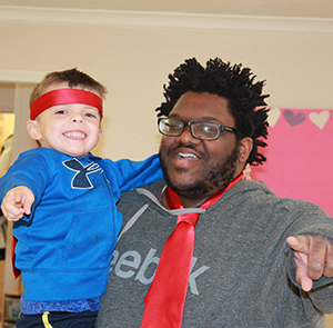 UNO Child Care Center student picked up by staff member and both pointing at the camera