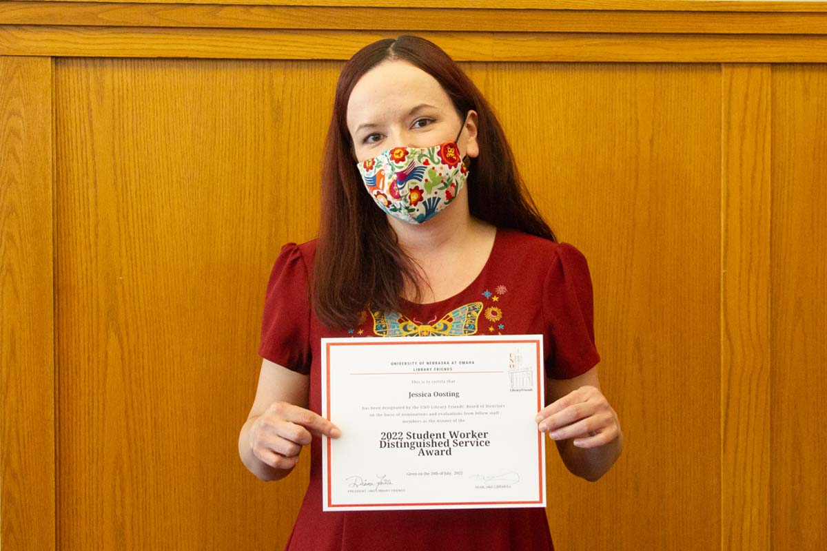 Jessica holding a certificate and mask, looking at the camera
