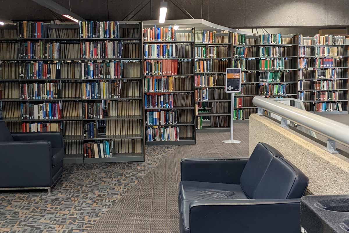 book stacks in a library with a silver sign that says 'quiet please' to the right