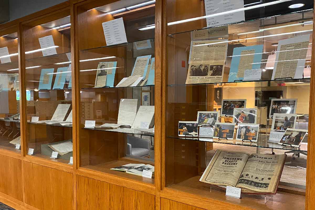 wooden and glass display cabinets with newspaper clippings, old photos, and old papers 