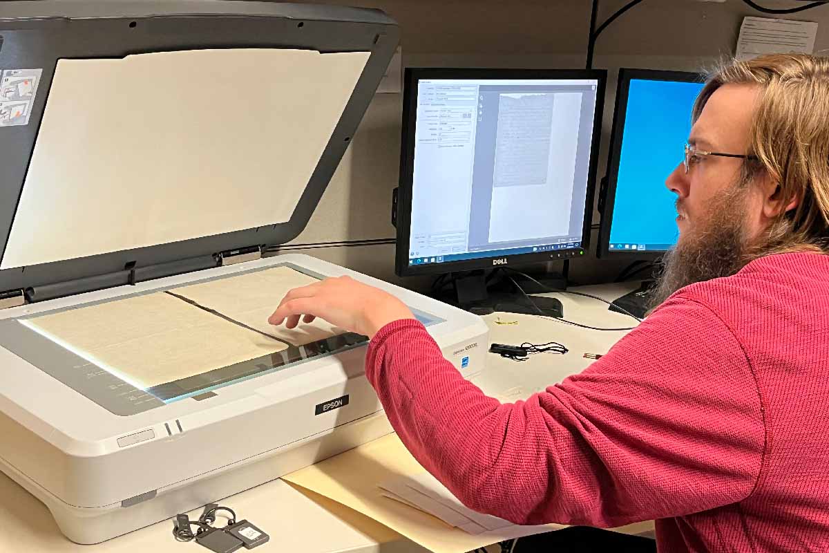 a man with a beard and glasses scanning old letters to a computer 