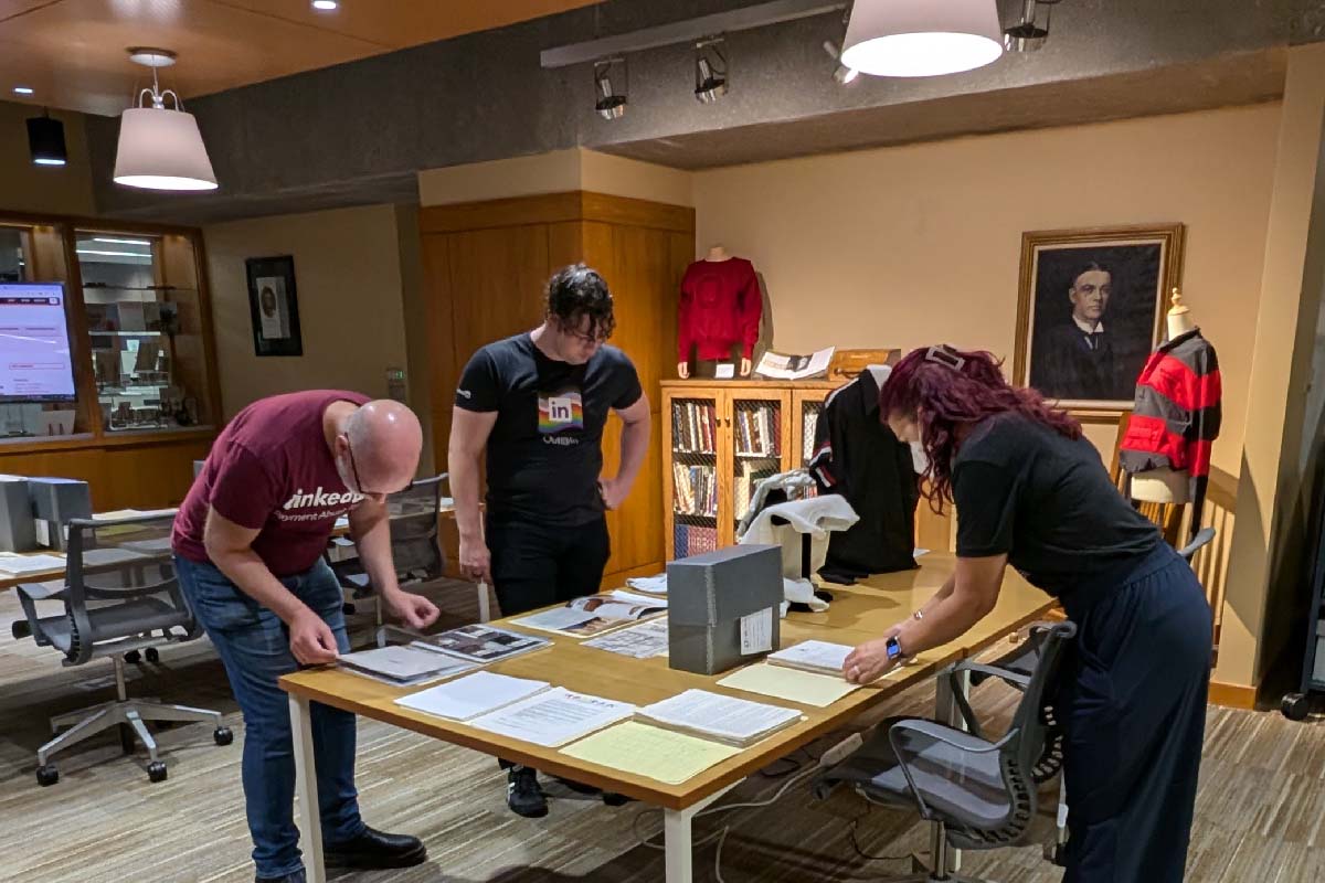 three people standing around a table looking at archival boxes and documents